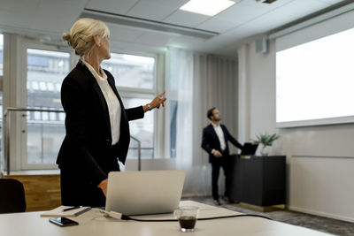 Businesswoman using laptop while discussing with colleague over flat screen during global conference in office