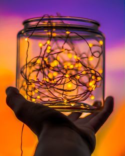 Cropped hand holding illuminated string lights in jar during sunset