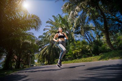 Low angle view of woman jumping on road against trees