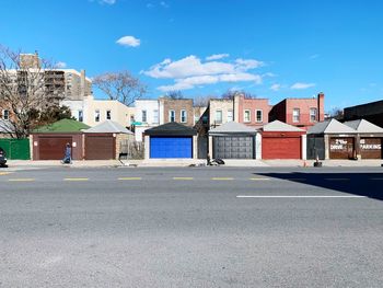 Road by buildings against blue sky