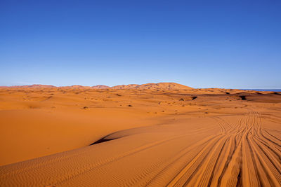 Amazing view of sand dunes with tyre marks in desert against clear sky