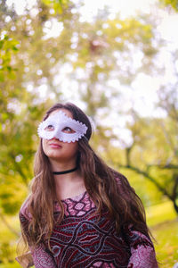 Young woman wearing venetian mask against trees