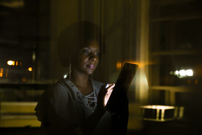 Businesswoman using tablet computer in dark office seen through glass