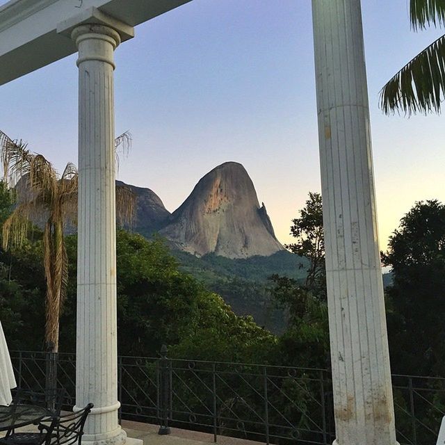 mountain, clear sky, built structure, tree, mountain range, architecture, tranquility, scenics, railing, landscape, nature, sunlight, tranquil scene, sky, beauty in nature, day, travel destinations, blue, connection, indoors