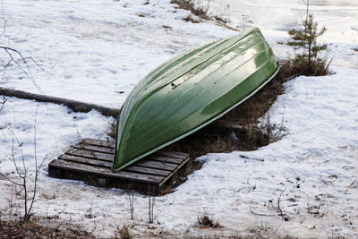 A green boat lying on shore in anticipation of summer