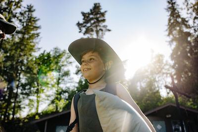 Low angle view of smiling boy wearing hat during sunny day at summer camp