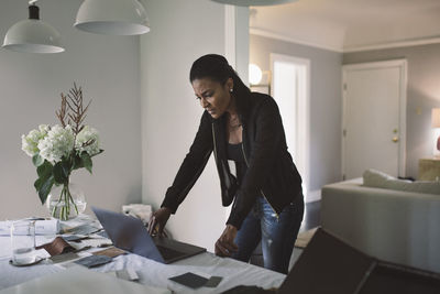 Worried businesswoman looking at laptop while standing by dining table at home office