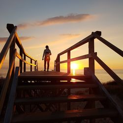 Silhouette woman standing on staircase against sky during sunset