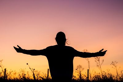 Silhouette woman standing with arms outstretched against sky during sunset