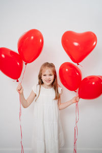 Portrait of smiling girl with red balloons against white background