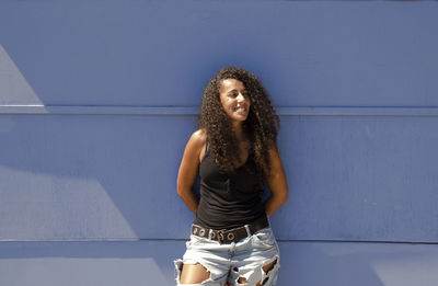 Full length of young arabic woman standing against blue wall in summer