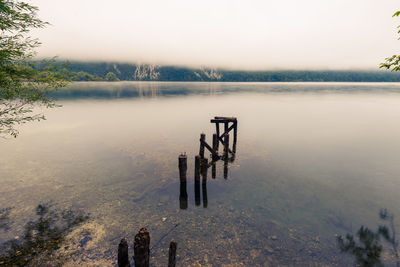 Wooden posts in lake against sky