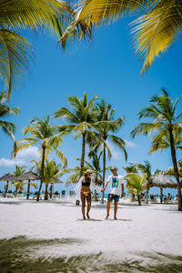 People by palm trees on beach against clear sky