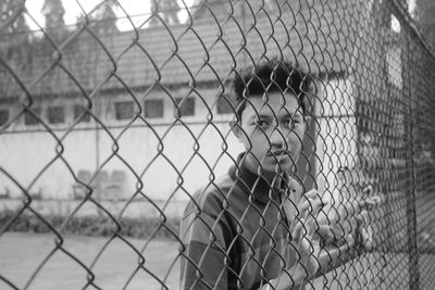 Rear view of man looking through chainlink fence