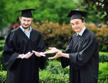 Portrait of woman wearing graduation gown standing in park