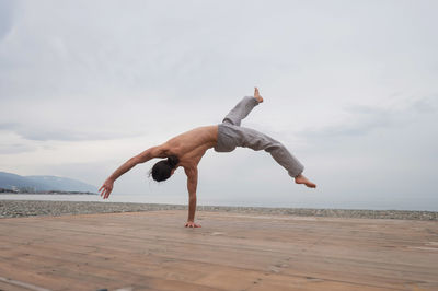 Shirtless caucasian man doing backflip on pebble beach