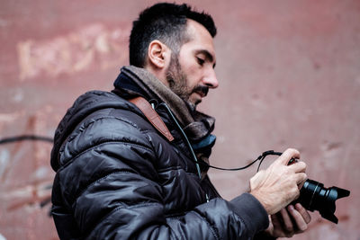 Low angle view of man holding camera against wall