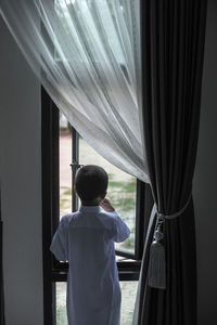 Rear view of boy looking through window