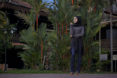 Full length of thoughtful young woman wearing hijab while standing against plants