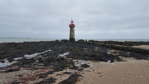 Lighthouse on beach by sea against sky