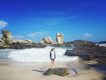 Man standing on rocks by sea against sky