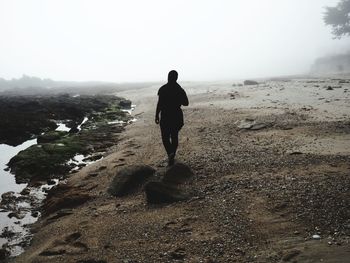 Silhouette man walking at beach during foggy weather