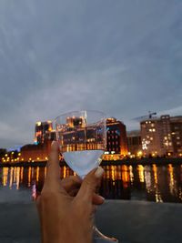 Cropped image of hand holding illuminated cityscape against sky