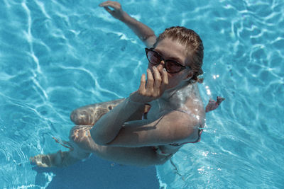 High angle portrait of young woman wearing sunglasses swimming in pool during sunny day