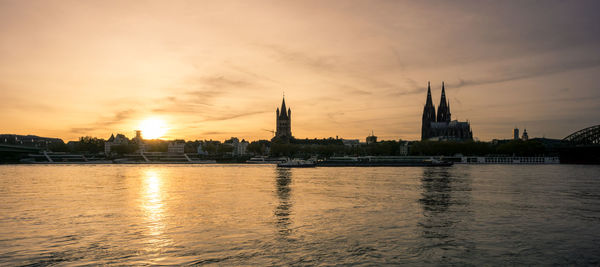 River by buildings against sky during sunset