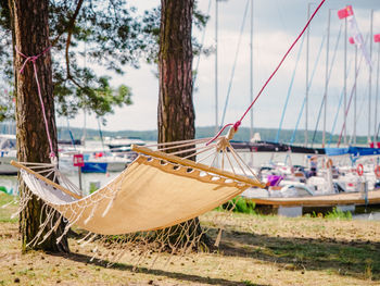 Boho style white linen hammock hanging between pine trees on a lakeshore with sailing boats port