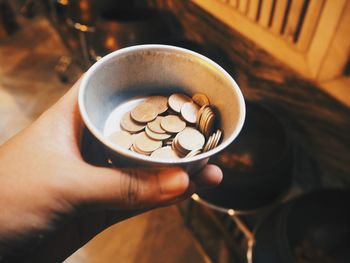 Cropped hand of person holding coins in container