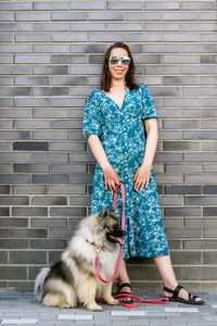 Stylish woman with fluffu dog standing near to bricks wall. 