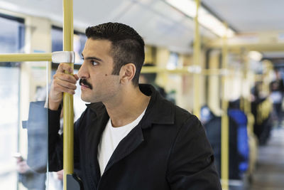 Young man leaning on pole in tram