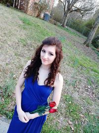 Portrait of young woman standing on grass against trees