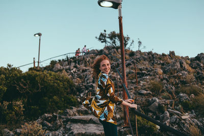 Portrait of young woman standing on rock against sky