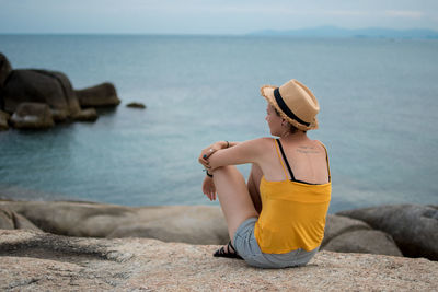 Young woman sitting on rock by sea