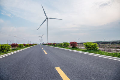 Road by wind turbines against sky