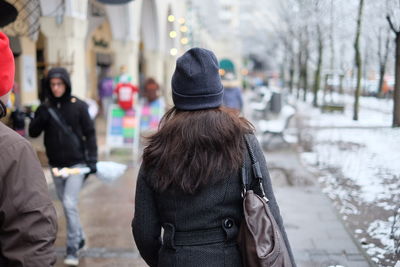 Rear view of woman in knit hat and jacket walking on footpath