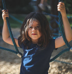 Portrait of a little caucasian girl stands on a rope swing holding on to the ropes with her hands