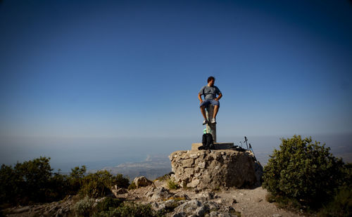 Man standing on rock against clear blue sky