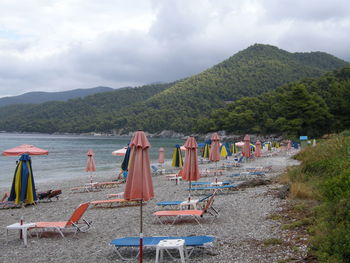 Closed parasols and deck chairs at beach against sky