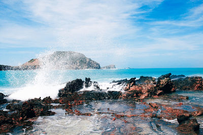 Sea waves splashing on rocks against sky