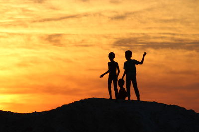 Silhouette of friends standing against orange sky