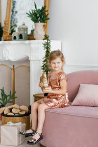 A child girl holds a wooden toy horse in her hands and sits on the sofa near a christmas tree