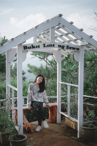 Young woman sitting by railing against plants