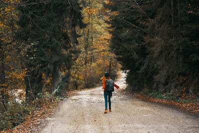 Rear view of woman walking on road in forest