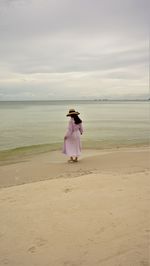 Woman standing on beach looking at sea against sky