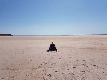 Man sitting on sand at beach against sky