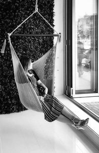 Rear view of woman sitting on hammock against window