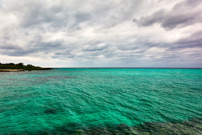 Scenic view of turquoise colored sea against cloudy sky